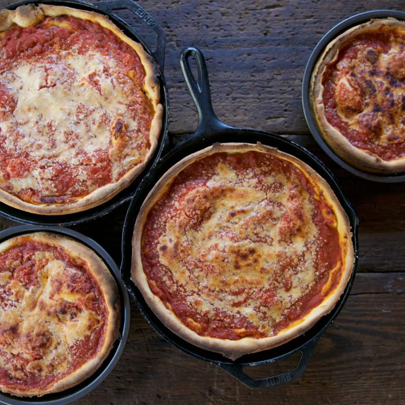Four pizzas in cast iron pans on a wooden surface