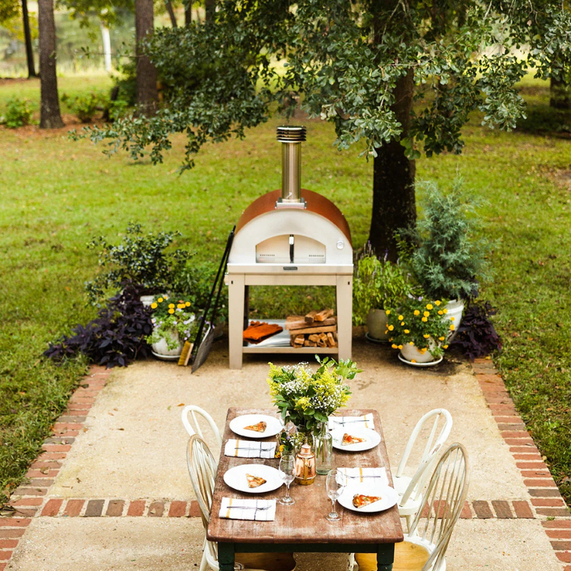 Outdoor setting with a pizza oven and dining table in a garden. Fontana Forni Marinara Pizza Oven Dual Fuel Countertop