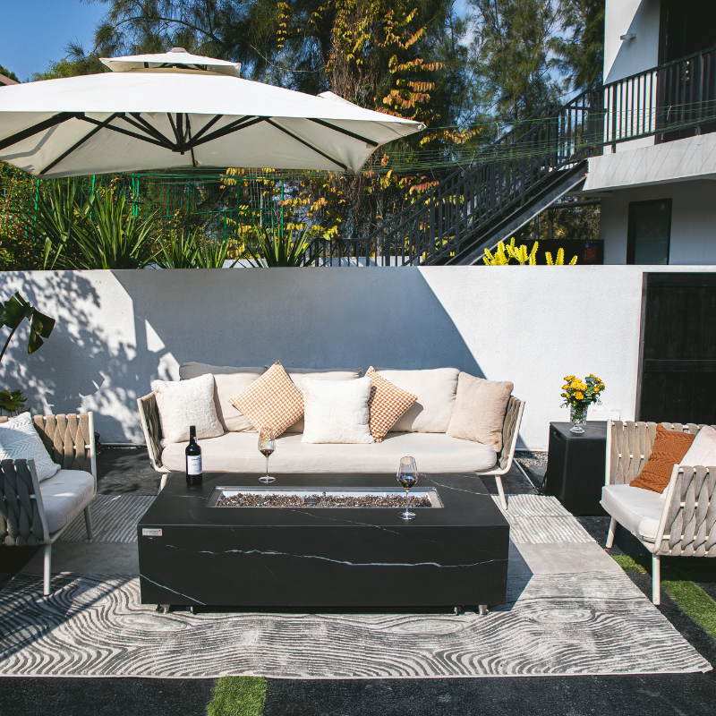 Outdoor patio setup with fire pit table, chairs, and umbrella. Elementi Fire Varna Black Marble Porcelain Fire Pit Table