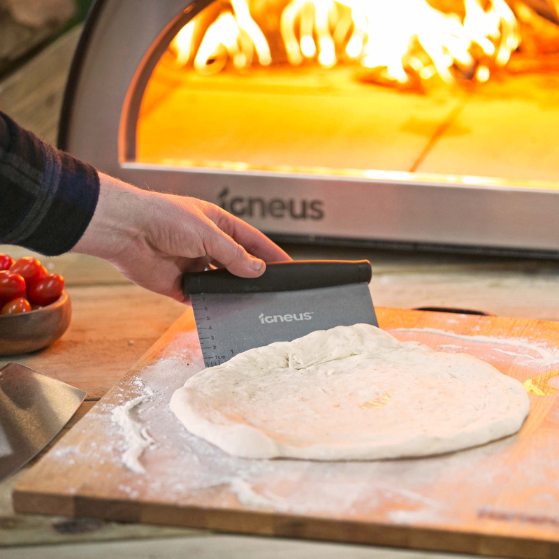 Person preparing pizza dough in front of a wood fired Igneus oven using the Igneus 5 part accessory set. Best igneus deal